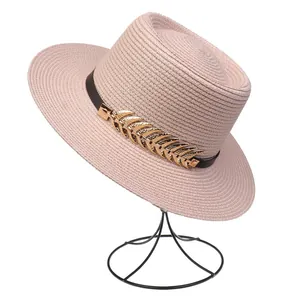 Detail of pink straw hat featuring a black leather band and golden metal leaf accents