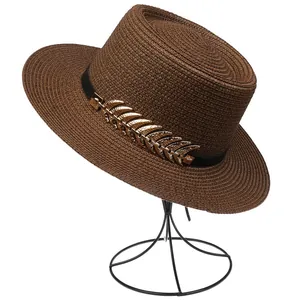 Detail of a brown straw sun hat featuring a black ribbon and gold metal leaf ornament