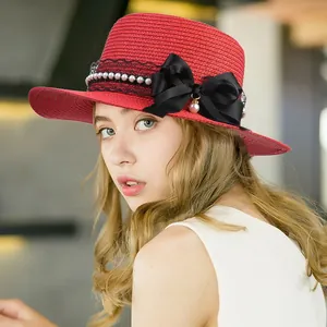 Elegant red woven straw sun hat with black lace, pearls, and a large satin bow