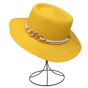 Detail of yellow straw hat with white rope band and gold chain accent on white background