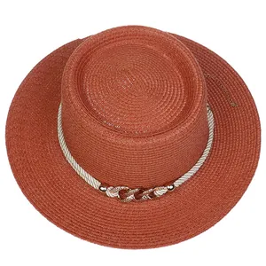 Macro detail of rust-red flat top straw hat with white rope and gold chain buckle