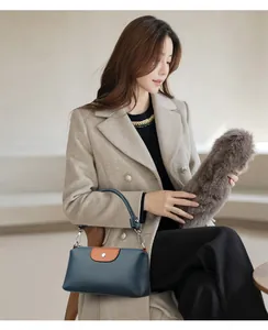 Modelo asiática en abrigo beige llevando un bolso de mano de cuero azul marino con detalle naranja.