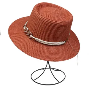 Detail of terracotta straw hat with woven white rope and decorative gold metal chain