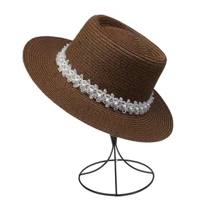 Detail eines braunen Strohhutes mit eleganter weißer Spitze und Perlenverzierungen