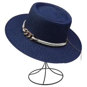 Detail of navy straw hat featuring decorative gold metal chain and white rope trim