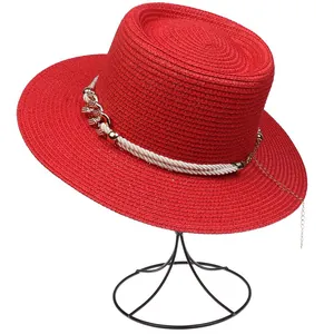 Macro detail of red straw sun hat with decorative white rope and gold chain elements