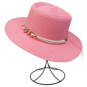Close-up of pink boater straw hat with white braided rope and golden chain detail