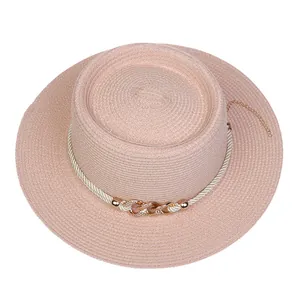 Detail of pink straw boater hat featuring a white rope band and gold chain accent