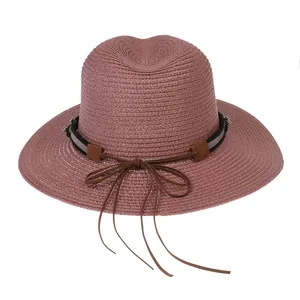 Gros plan sur un chapeau panama en paille rose avec ruban marron et perle en métal