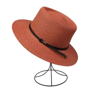 Close-up of brick red straw sun hat with black leather braided band and bronze buckle