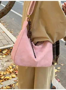Pink suede hobo bag with gold ring and heart charm shown on a model in autumn setting