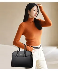 Détail d'un sac à main en cuir noir grainé avec boucle dorée porté par un mannequin