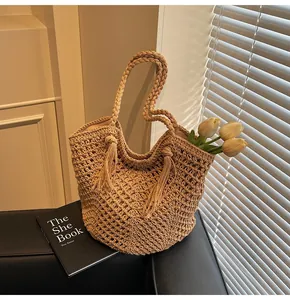 Detail view of a woven beige tote bag with fringe tassels and hand-woven hollow pattern