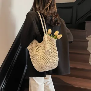 Handcrafted cream crochet tote bag with tassels shown on a shoulder in a modern setting