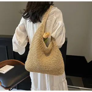 Detail of a large woven straw hobo bag being worn by a model in a minimal interior