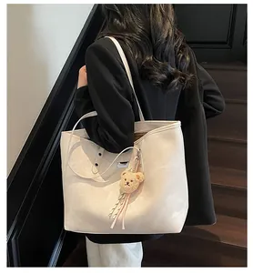 Detail of cream leather tote bag featuring a cute plush bear charm and striped tassel