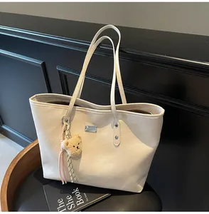 Detail of off-white large tote bag on a black chair showing metal logo and bear charm
