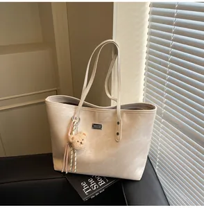 Detailed macro view of beige faux leather tote bag with branded metal logo and bear pendant