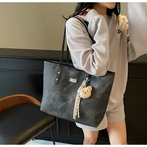 Detail view of large dark grey tote bag with bear charm on a grey textured sweatshirt