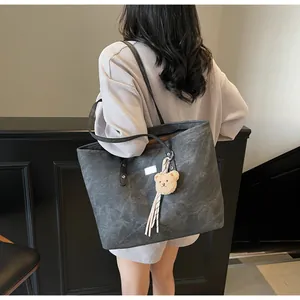 Large dark grey tote bag with bear charm shown on model's shoulder in minimal setting