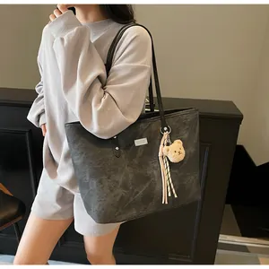 Detail view of large grey tote bag showing stone texture, bear charm, and stripe tassel