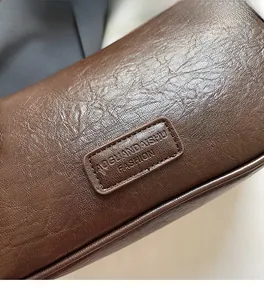 Detail of soft brown pebble leather texture and stitched logo patch on handbag