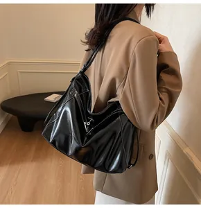 Détail du sac hobo en cuir brillant noir avec coutures blanches et boucle argentée