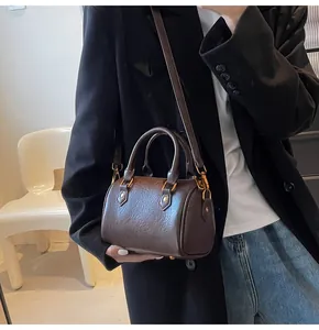 Detail of a dark brown Boston bag featuring pebbled texture and gold-tone metal hardware