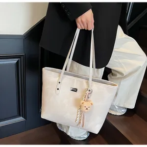 Detail of cream leather tote bag featuring a metal logo plate and cute teddy bear charm