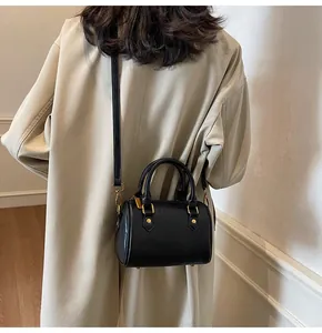 Detail of black Boston cylinder bag with gold hardware worn over a khaki trench coat