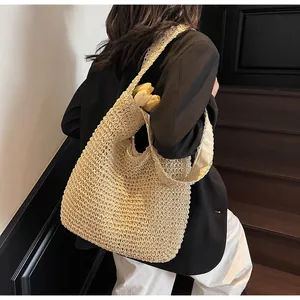 Detailed side view of beige hand-woven straw tote bag with wide strap and floral accent