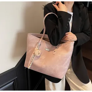 Close-up of pink tote bag showing faux suede texture, metal logo, and plush bear charm
