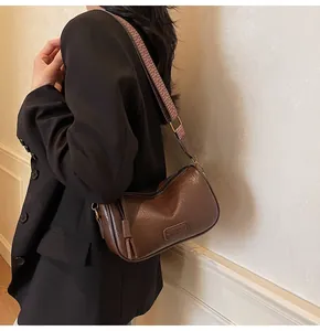 Detail of vintage brown shoulder bag featuring wide geometric woven strap on model