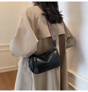 Detail of black glossy crossbody bag with geometric wide strap on trench coat