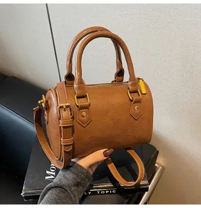 Close-up of brown Boston bag with textured leather, gold hardware, and adjustable strap