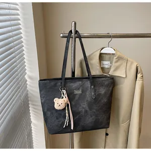 Close-up of black retro matte tote bag with plush bear charm and striped rope detail