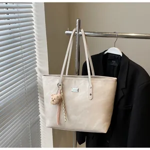 Detail of cream large tote bag with brown bear charm and metallic brand plaque