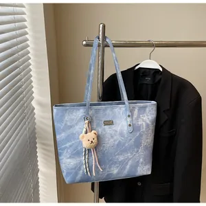Detail of light blue denim tote bag with plush bear charm and metallic brand plaque