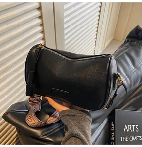 Detail view of black cylinder bag with purple textured wide strap and golden hardware