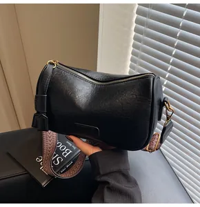 Close-up of black retro cylinder bag featuring wide textured strap and gold hardware