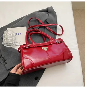 Detail of red glossy leather handbag with triangle metal logo and adjustable strap
