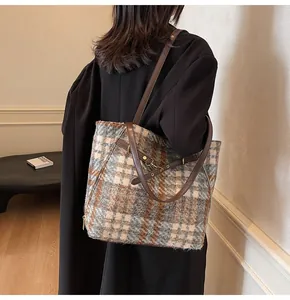 Detail einer großen Vintage-Karo-Tasche mit Lederriemen an einem Model im schwarzen Mantel