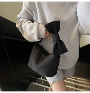 Chic black handbag with oversized bow detail held by model on a modern staircase