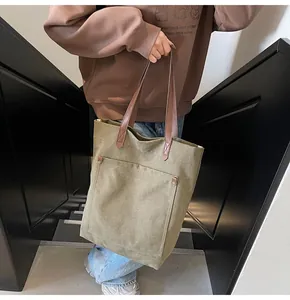 Detalle del bolso tote de lona verde oliva con remaches metálicos y asa de cuero marrón