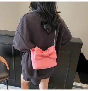 On-body view of a small pink crossbody bag featuring a large bow and chain strap