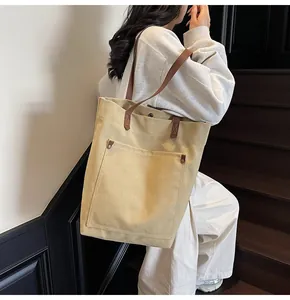Detalle del bolso tote de lona caqui con asas de cuero marrón y bolsillo con remaches