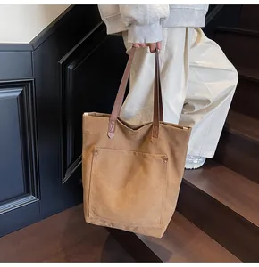 Detalle de bolso tote de lona con asa de cuero, remaches metálicos y bolsillo frontal