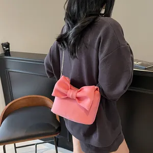 Pink ribbon crossbody bag with silver chain strap shown in a stylish cafe setting