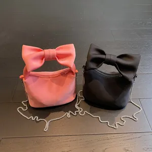 Pink and black bow tote bags with silver chain straps on dark wooden background