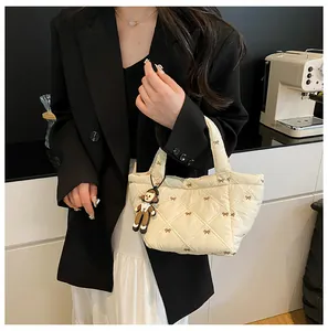Close-up of beige quilted bucket bag with bow embroidery and a cute doll pendant